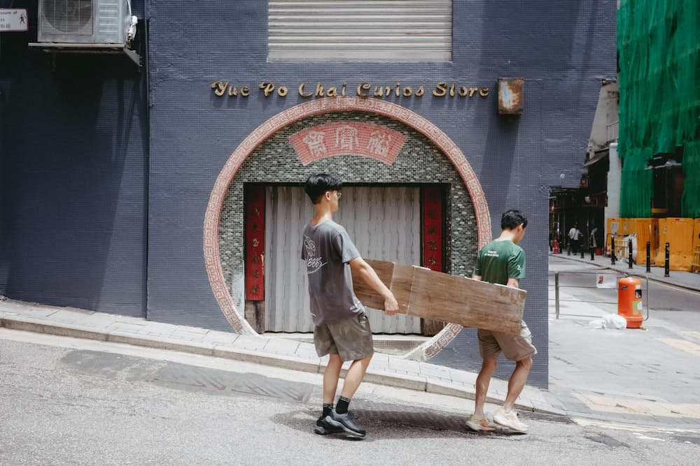 Two people carrying a large cardboard box down a city street